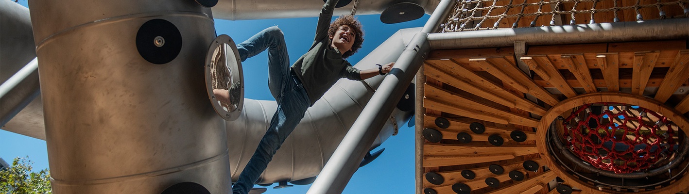 A cheerful boy with curls climbs on the stainless steel octopus in La Pegaso Park in Barcelona