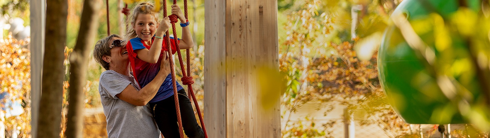 Mother helps her daughter down from a rope climbing wall, autumn scene