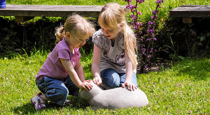 Two children stroking a concrete cat in the garden