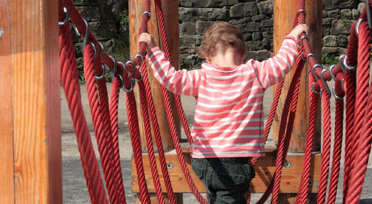 Girl holding on to red ropes to get over bridge